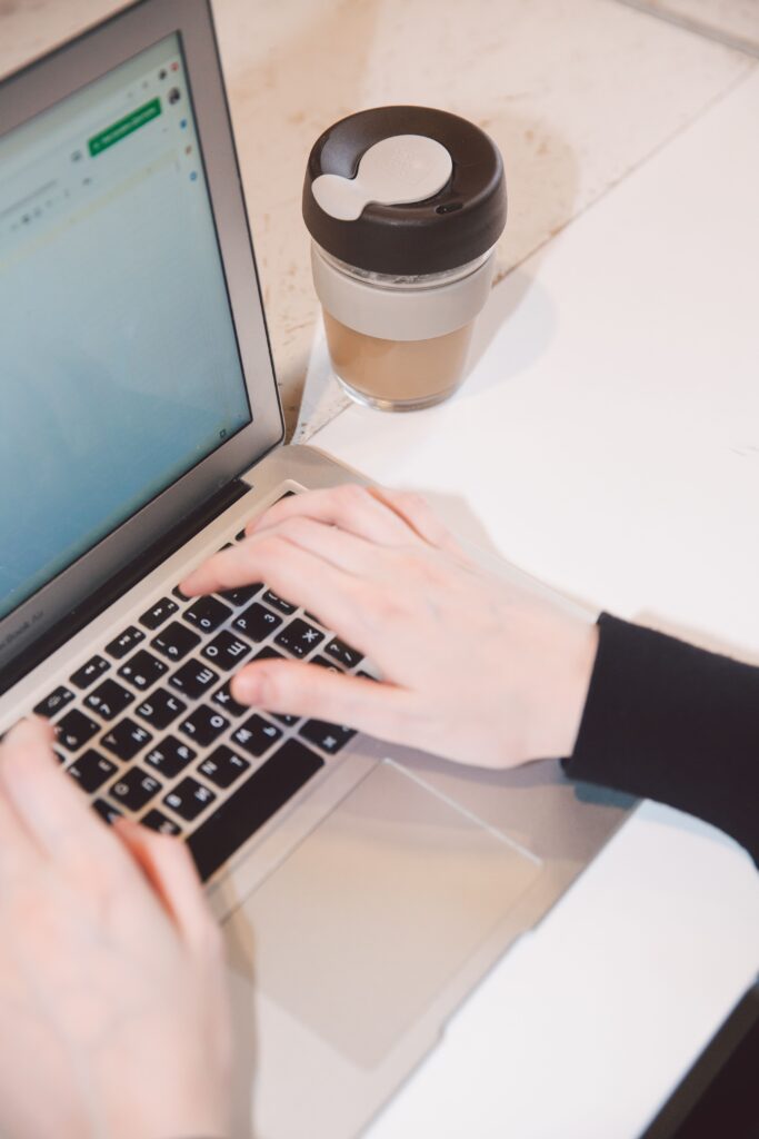 Hands typing on a laptop with a coffee cup nearby, representing remote work and technology.